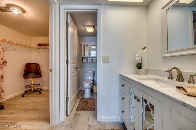 bathroom featuring wood finished floors, baseboards, vanity, toilet, and a spacious closet