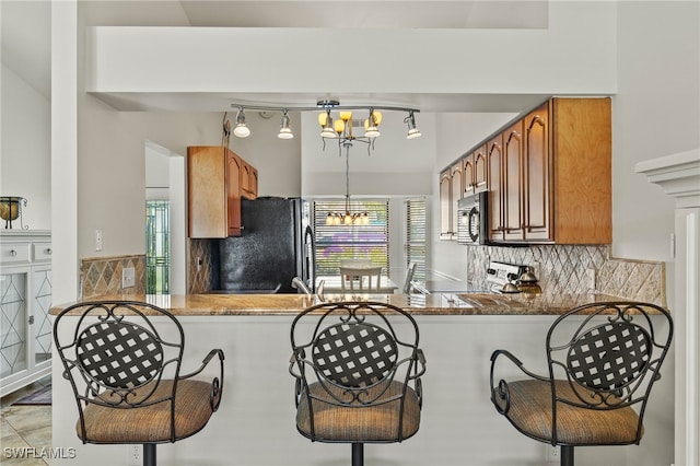 kitchen featuring pendant lighting, kitchen peninsula, a chandelier, and black appliances