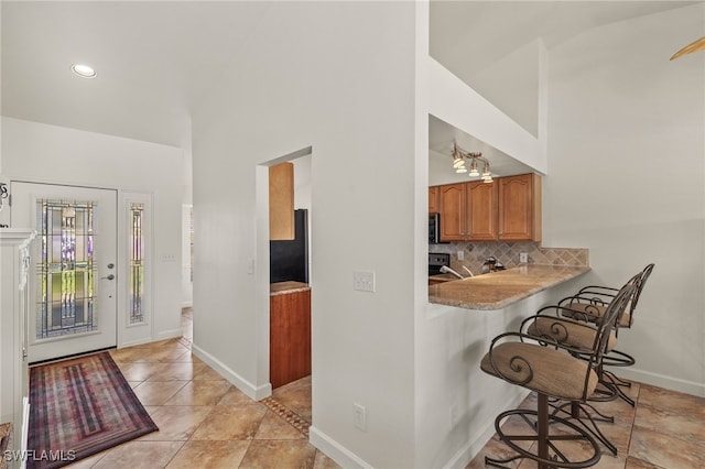 kitchen featuring a breakfast bar, kitchen peninsula, backsplash, and a towering ceiling