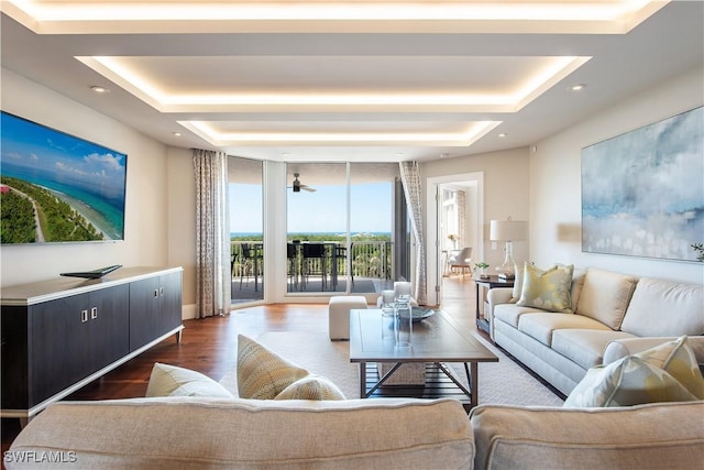 living room with ceiling fan, dark wood-type flooring, a wall of windows, and a tray ceiling