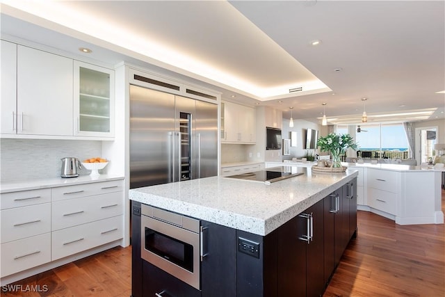 kitchen featuring light stone counters, stainless steel microwave, a kitchen island, black electric stovetop, and white cabinets