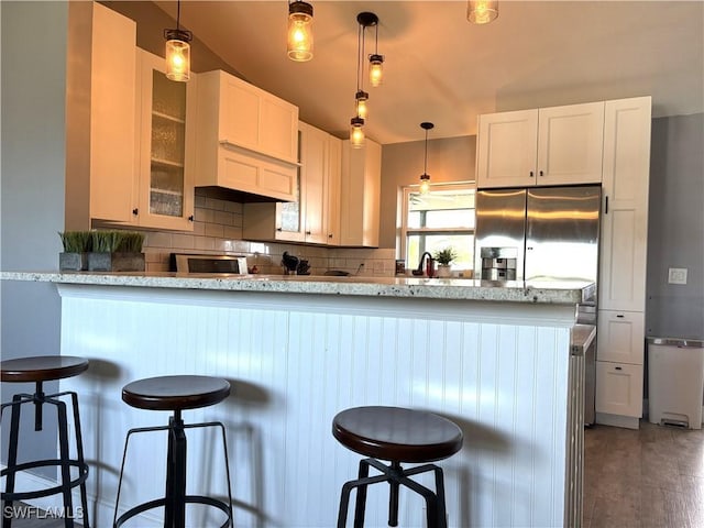 kitchen featuring a breakfast bar, hanging light fixtures, light stone countertops, white cabinets, and stainless steel fridge with ice dispenser