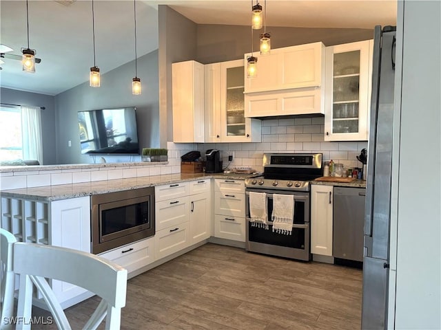 kitchen with pendant lighting, lofted ceiling, white cabinets, light stone counters, and stainless steel appliances