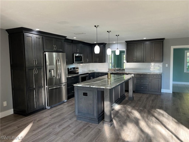 kitchen with appliances with stainless steel finishes, a breakfast bar, hanging light fixtures, a center island, and light stone countertops