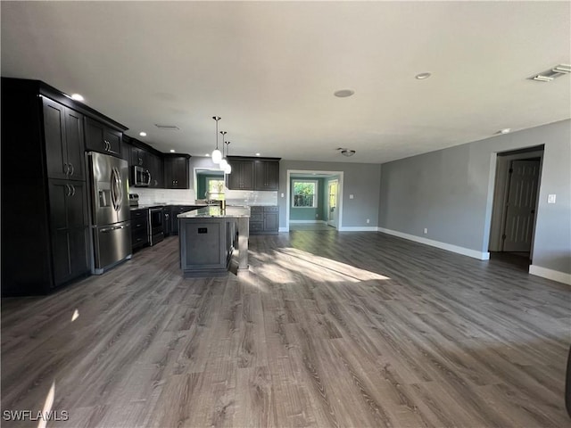 kitchen featuring pendant lighting, appliances with stainless steel finishes, dark hardwood / wood-style floors, tasteful backsplash, and a center island with sink