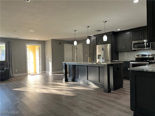 kitchen featuring tasteful backsplash, light stone counters, decorative light fixtures, an island with sink, and stainless steel appliances