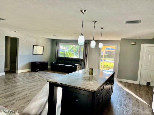 kitchen with light stone counters, hanging light fixtures, hardwood / wood-style floors, and a center island