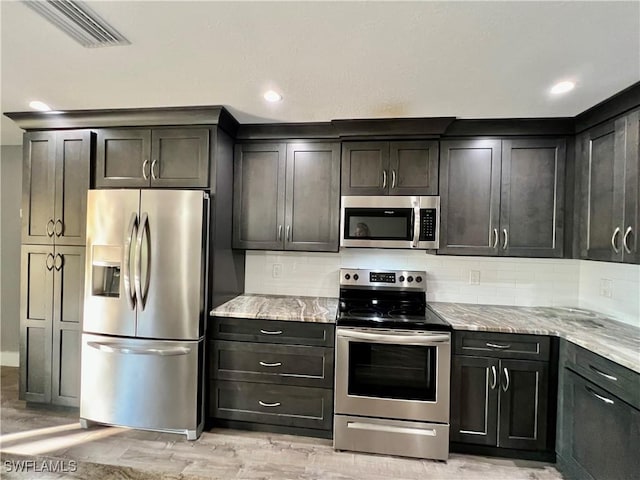 kitchen with light stone countertops, decorative backsplash, stainless steel appliances, and light hardwood / wood-style floors