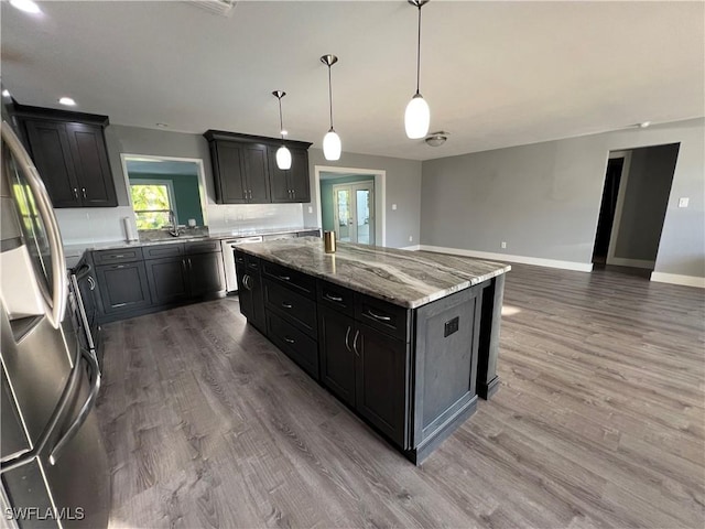 kitchen featuring stainless steel refrigerator, hardwood / wood-style floors, light stone countertops, a kitchen island, and decorative light fixtures