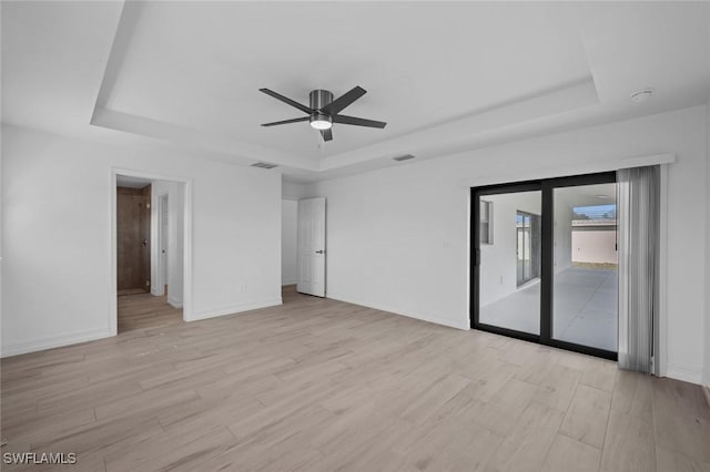 spare room with a tray ceiling, light hardwood / wood-style floors, and ceiling fan