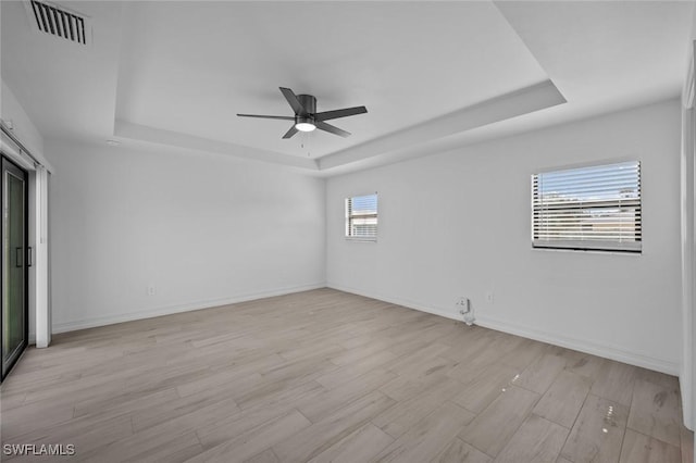 unfurnished room with ceiling fan, light wood-type flooring, and a tray ceiling