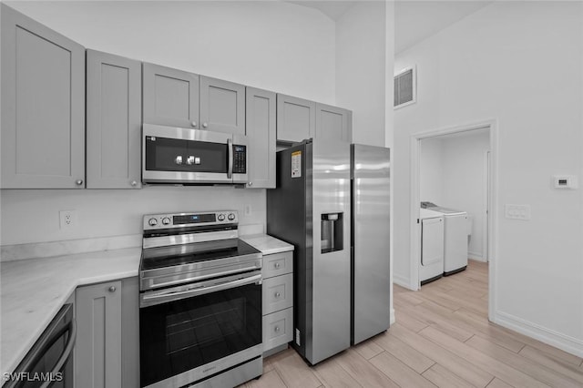 kitchen featuring appliances with stainless steel finishes, a towering ceiling, gray cabinetry, and separate washer and dryer