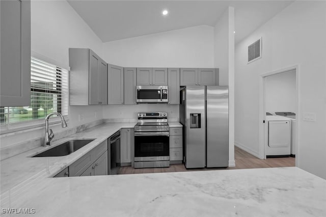 kitchen with sink, washer and clothes dryer, light hardwood / wood-style flooring, gray cabinetry, and stainless steel appliances