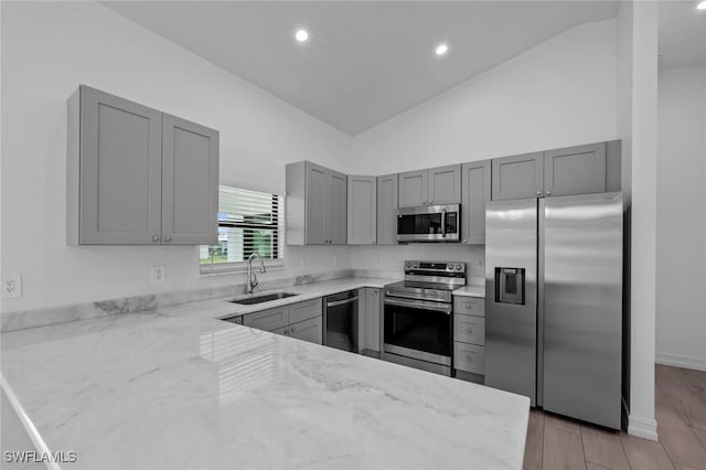 kitchen featuring sink, light wood-type flooring, appliances with stainless steel finishes, kitchen peninsula, and light stone countertops