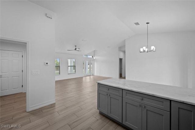 kitchen with lofted ceiling, light stone counters, light wood-type flooring, gray cabinets, and pendant lighting