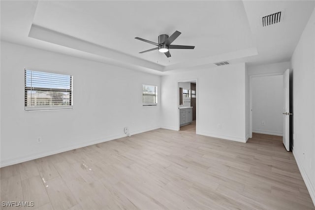 unfurnished bedroom featuring connected bathroom, a tray ceiling, light hardwood / wood-style flooring, and ceiling fan