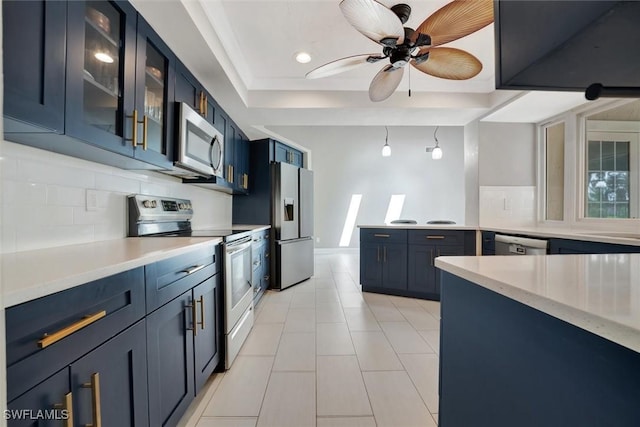 kitchen featuring blue cabinetry, appliances with stainless steel finishes, a raised ceiling, ceiling fan, and decorative backsplash