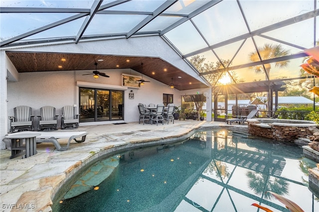 pool at dusk with a lanai, a patio, ceiling fan, and an in ground hot tub