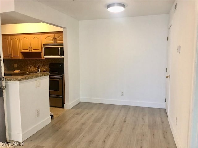 kitchen featuring tasteful backsplash, range with electric stovetop, dark stone countertops, and light wood-type flooring