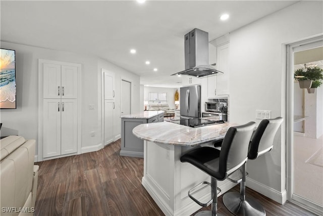 kitchen with a kitchen island, a breakfast bar, stainless steel fridge, island exhaust hood, and light stone countertops