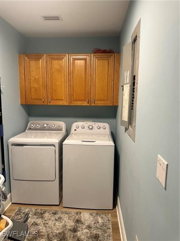 laundry area featuring cabinets, washing machine and clothes dryer, electric panel, and light wood-type flooring