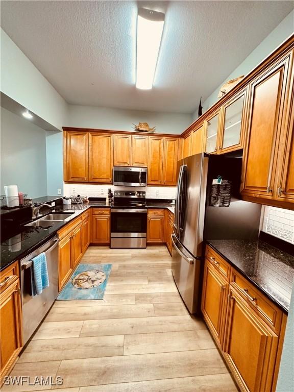 kitchen featuring dark stone countertops, sink, stainless steel appliances, and light wood-type flooring