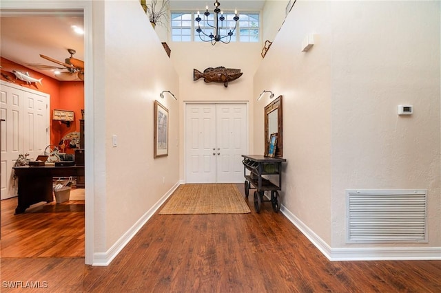 hall featuring a notable chandelier, wood-type flooring, and a high ceiling