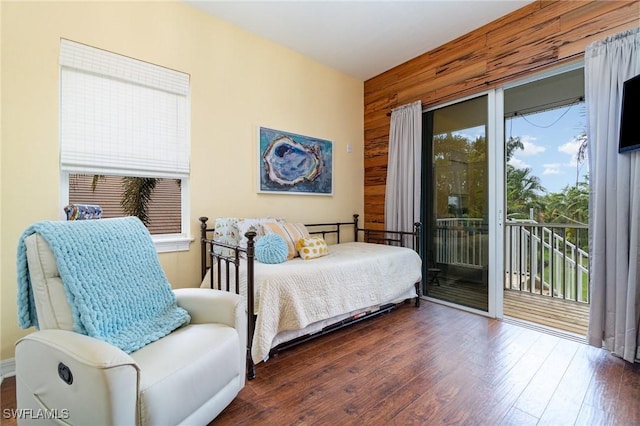 bedroom featuring multiple windows, dark hardwood / wood-style flooring, wooden walls, and access to outside