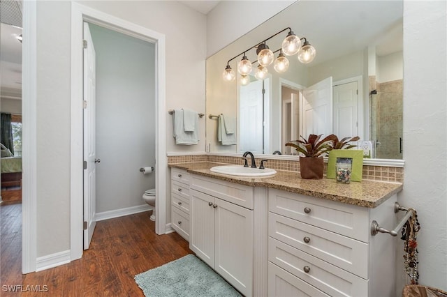 bathroom with hardwood / wood-style floors, a shower with shower door, decorative backsplash, vanity, and toilet