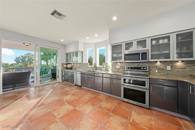 kitchen featuring appliances with stainless steel finishes, sink, backsplash, light tile patterned floors, and light stone counters