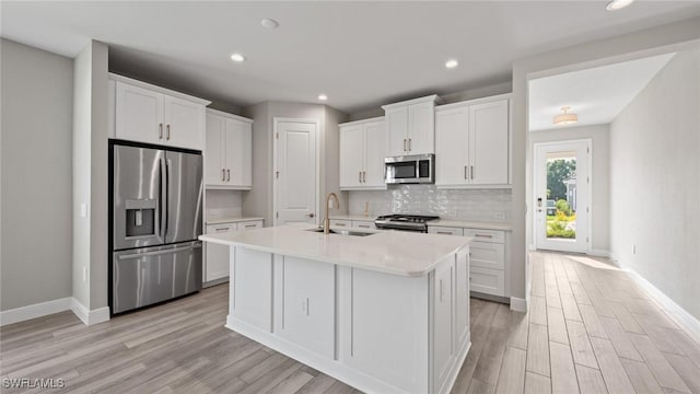 kitchen featuring sink, stainless steel appliances, tasteful backsplash, an island with sink, and white cabinets