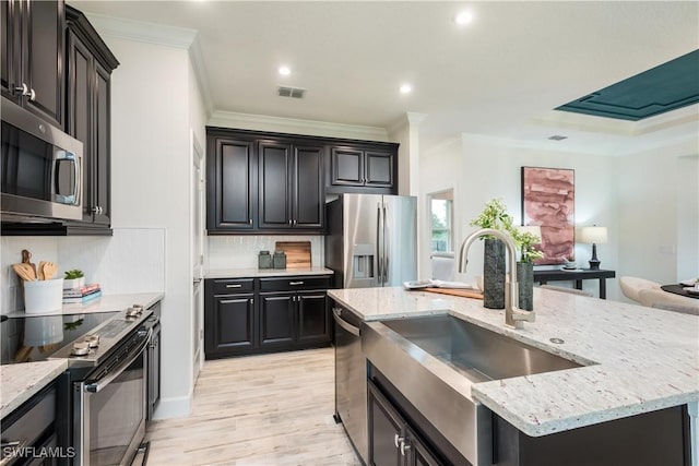 kitchen with a sink, visible vents, ornamental molding, appliances with stainless steel finishes, and a center island with sink