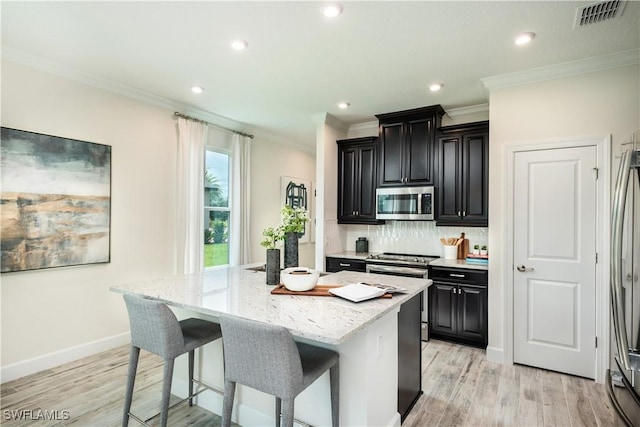 kitchen featuring visible vents, a kitchen island, appliances with stainless steel finishes, a kitchen breakfast bar, and dark cabinets