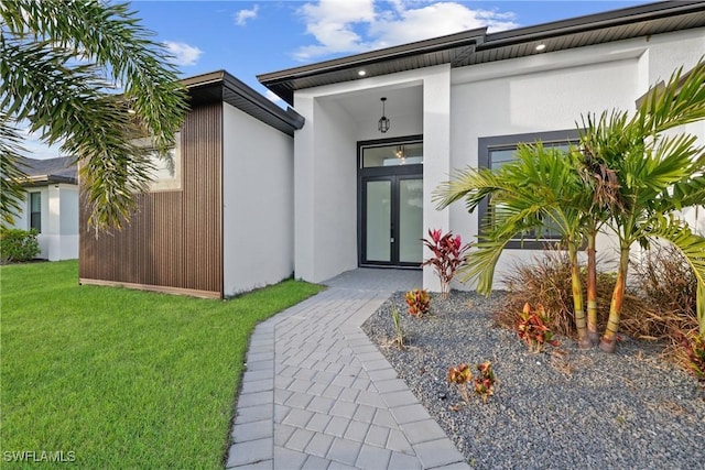 view of exterior entry with a yard, french doors, and stucco siding