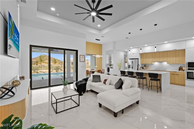 living area featuring marble finish floor, a high ceiling, a tray ceiling, and ceiling fan