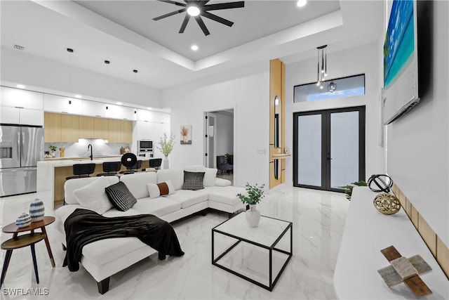 living area with marble finish floor, a tray ceiling, french doors, a high ceiling, and ceiling fan