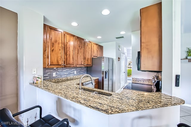 kitchen with a breakfast bar area, light stone counters, range, stainless steel fridge with ice dispenser, and kitchen peninsula