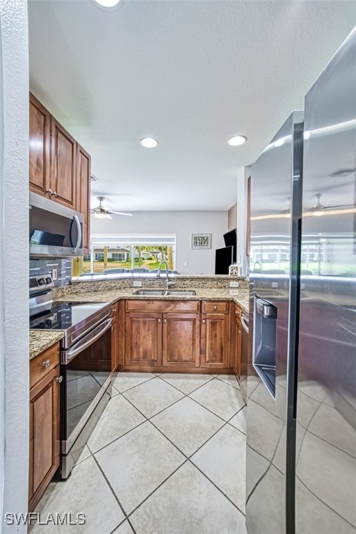 kitchen with sink, light tile patterned floors, ceiling fan, light stone counters, and stainless steel appliances