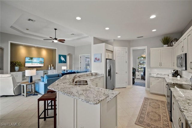 kitchen featuring sink, stainless steel appliances, white cabinets, and a center island with sink