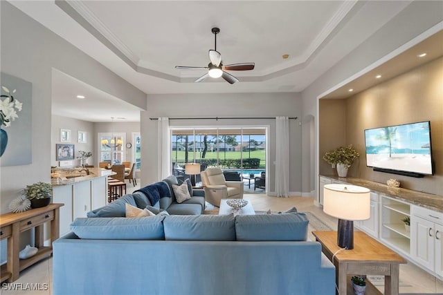 living room featuring ceiling fan, ornamental molding, and a raised ceiling