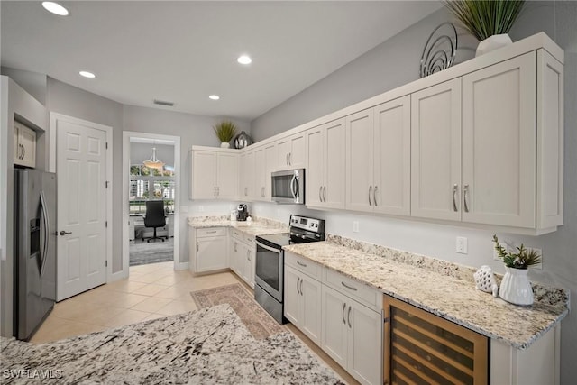 kitchen featuring stainless steel appliances, white cabinetry, beverage cooler, and light stone counters