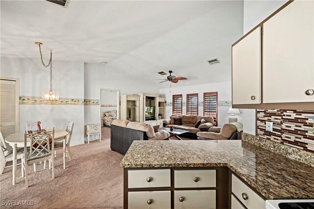 kitchen featuring lofted ceiling, white cabinets, ceiling fan with notable chandelier, light colored carpet, and dark stone counters