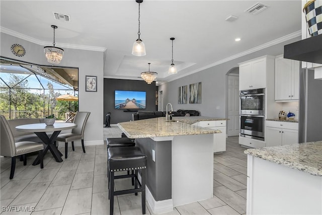 kitchen featuring white cabinetry, hanging light fixtures, stainless steel appliances, light stone countertops, and an island with sink