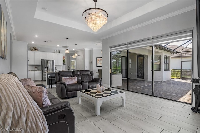 living room with a raised ceiling, crown molding, and a chandelier