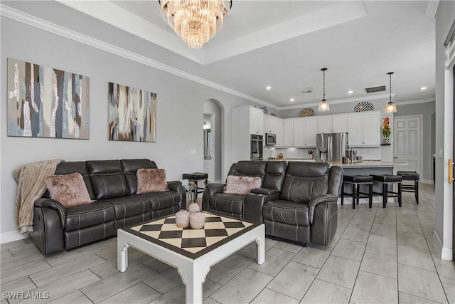 living room with crown molding, a tray ceiling, and an inviting chandelier