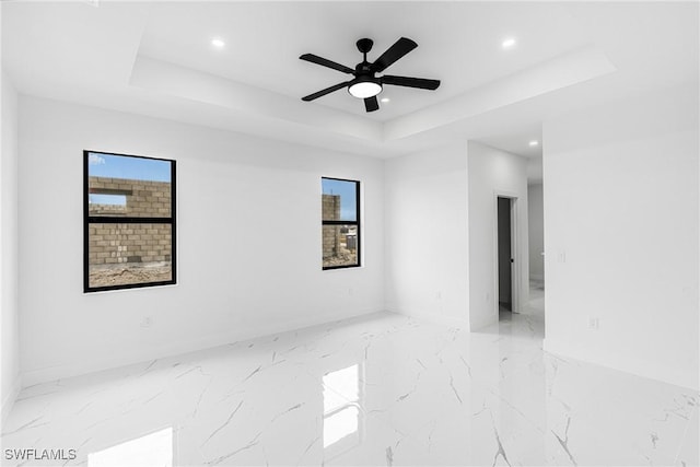 empty room with ceiling fan, plenty of natural light, and a tray ceiling