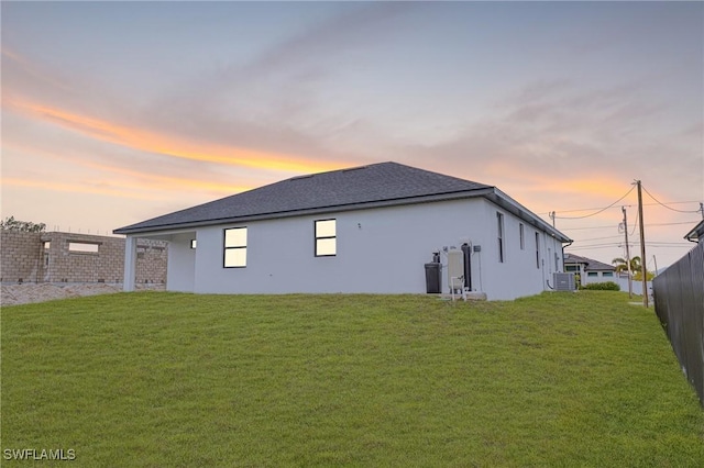 back house at dusk featuring a lawn and central air condition unit