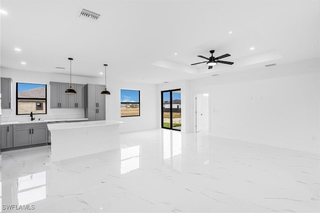 kitchen featuring sink, decorative light fixtures, gray cabinets, a raised ceiling, and a wealth of natural light