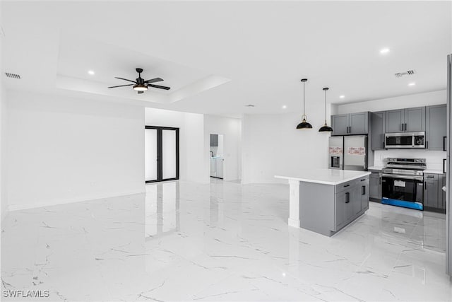 kitchen with appliances with stainless steel finishes, gray cabinetry, a center island, decorative light fixtures, and a raised ceiling