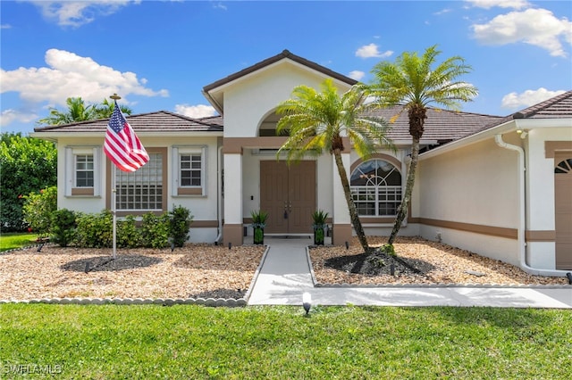 view of front of property with stucco siding, a front yard, and a tiled roof